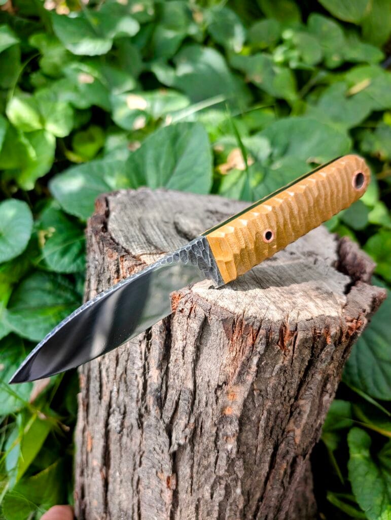 “Full side view of the Mowgli knife in K110 steel with mirror finish and textured black wood handle.”